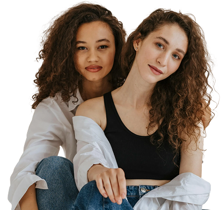 Two women with curly hair sitting close together, wearing casual clothing and looking at the camera.